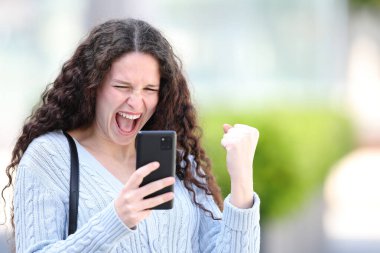 Caddede cep telefonu kullanan heyecanlı kadın.