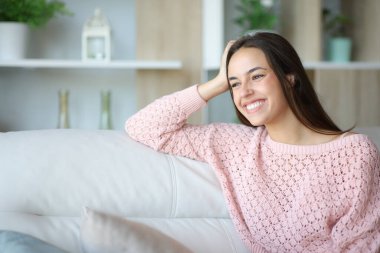 Mükemmel gülüşü olan mutlu bir kadın evdeki bir kanepede oturuyor.