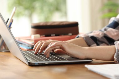 Evdeki ahşap bir masada dizüstü bilgisayarda yazan öğrenci ellerini kapat.