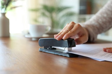 Evdeki ahşap masaya kağıtları zımbalayan bir kadının yakın çekimi.