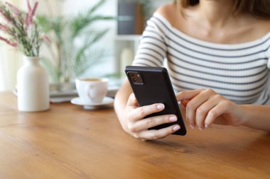 Evdeki ahşap masada mobie telefon kullanan bir kadının elleri.