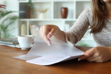 Evdeki ahşap masaya şeffaf plastik dosya cüzdanına kağıt çarşaf koyan bir kadının ellerini kapatın.