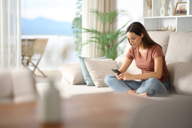 Kanepede oturan ciddi bir kadın. Evin içinde cep telefonu kullanıyor.