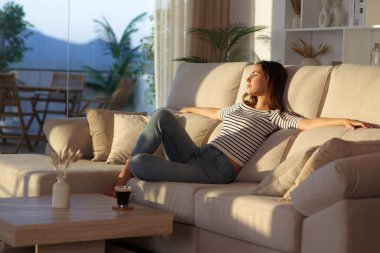 Rahat bir kadın kanepede oturup evdeki pencereden dışarı bakmayı düşünüyor.