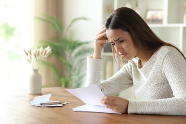 Evdeki ahşap masada mektup okuyan üzgün kadın.