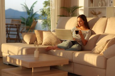 Gün batımında dizüstü bilgisayar kullanarak kahve içen bir kadın.