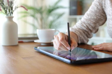 Evdeki tahta masada tablet ve dijital kalem kullanan bir kadının portresini kapat.