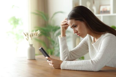 Endişeli kadın evin içindeki ahşap bir masada cep telefonunu kontrol ediyor.