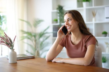 Evdeki mutlu kadın ahşap bir masada telefonla arıyor.