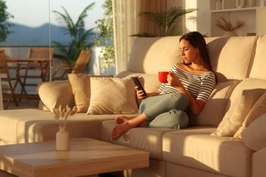 Rahat bir kadın koltukta oturmuş kırmızı bardaktan kahve içiyor.