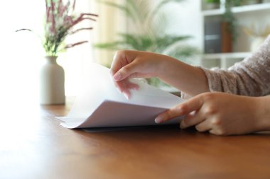 Kadın elinin, evdeki ahşap masanın üstündeki şeffaf plastik dosyaya kağıt çarşaf koyması.