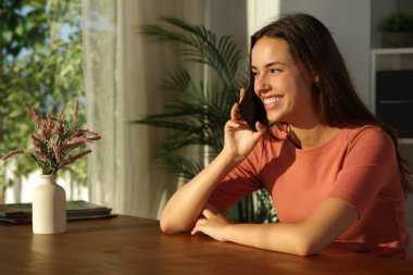 Mutlu kadın telefonda konuşuyor, gün batımında evde oturuyor.