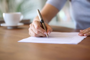 Ev sahibinin, kağıt imzalamak için ahşap masa üzerindeki kalemle kapanışı.