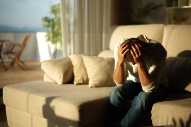 Üzgün ve çaresiz adam gün batımında evdeki kanepede oturuyor.