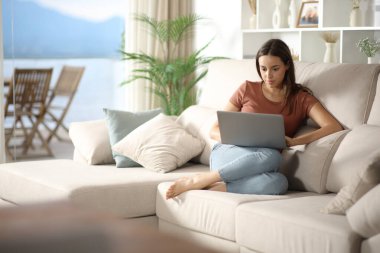 Ciddi bir kadın evdeki koltukta otururken kişisel bilgisayar kullanıyor.
