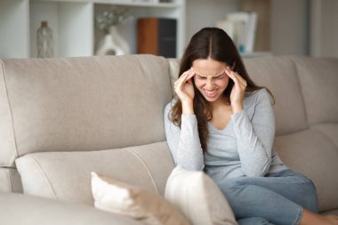 Migren krizi geçiren bir kadın evde bir kanepede tek başına oturuyor.