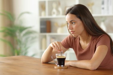 Kafası karışık bir kadın kahvesini karıştırıyor. Evdeki masaya bakıyor.