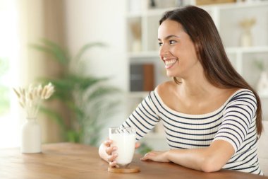 Bir bardak süt tutan mutlu kadın evdeki bir masaya bakıyor.