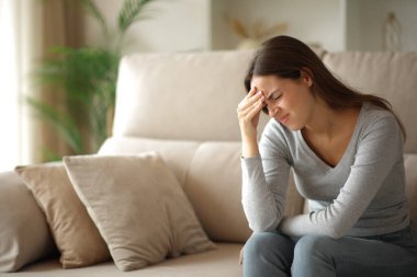 Başı ağrıyan stresli bir kadın evde bir kanepede oturup şikayet ediyor.