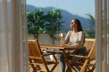 Terasta oturup kahve içen rahat bir kadın evde temiz hava soluyor.
