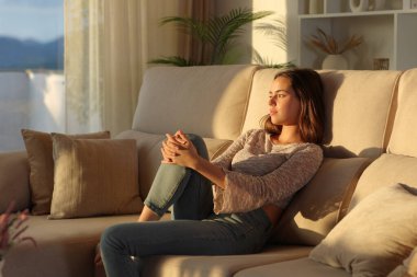 Gün batımında düşünceli bir kadın kanepeye oturmuş başka tarafa bakıyor.