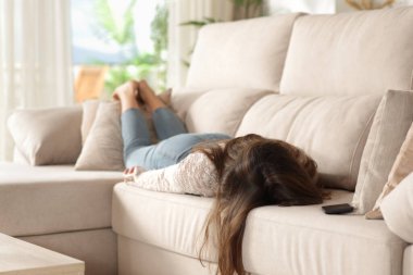 Yorgun bir kadın kanepede uzanıp evinde tuhaf bir şekilde dinleniyor.