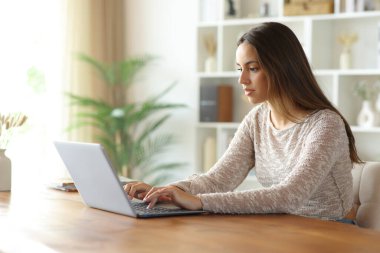 Evdeki ciddi kadın ahşap masadaki kişisel bilgisayarını kullanıyor.