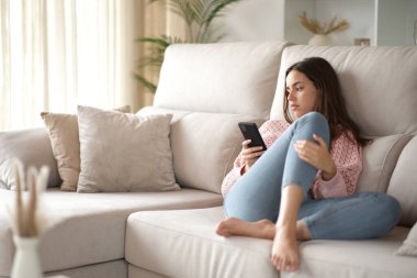 Ciddi bir kadın evdeki koltukta cep telefonunu kontrol ediyor.