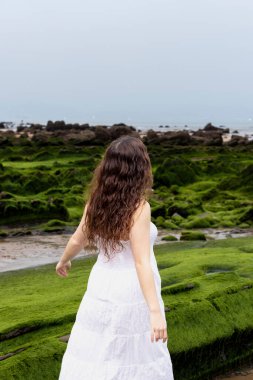 Kadın sahilde geri geri yürüyor.