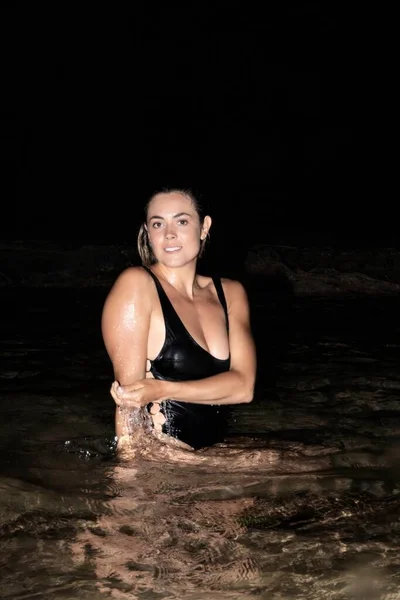 真夜中に海岸の水の中に座っているブロンドの女性がカメラを見て 休暇のコンセプト — ストック写真