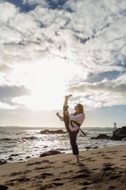 Siyah kuşaklı kız sahilde tekvando yapıyor.