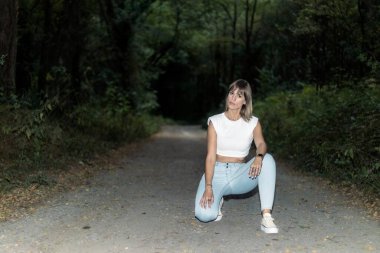 Thoughtful beautiful woman wearing jeans squatting in the woods