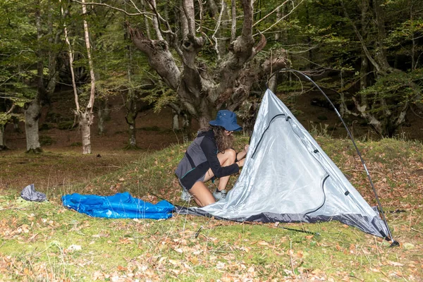woman with outdoor gear setting up his tent in a clearing after a day of hiking in the woods