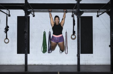 toes to bar woman pull ups 2 bars workout exercise at gym.Woman working out on cross bars in a gym hanging from extended arms during a fitness workout.