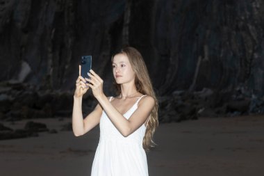 Woman holding mobile phone at sunset. Young woman taking photos with her cell phone in a beautiful amazing sunset over sea. Taking a picture on a smartphone during a vacation