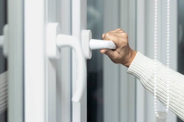 Close-up of a womans hand opens a plastic white window to ventilate.