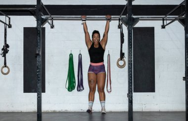 toes to bar woman pull ups 2 bars workout exercise at gym.Woman working out on cross bars in a gym hanging from extended arms during a fitness workout.