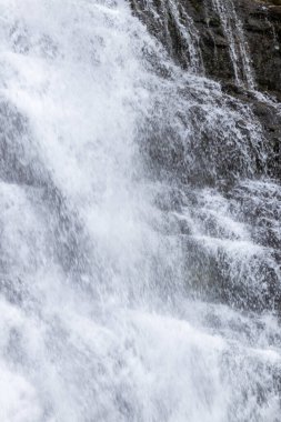 Köpüklü, beyaz bir şelalenin karanlık, sarp kayalıklardan aşağı yuvarlanışının yakın plan fotoğrafı.