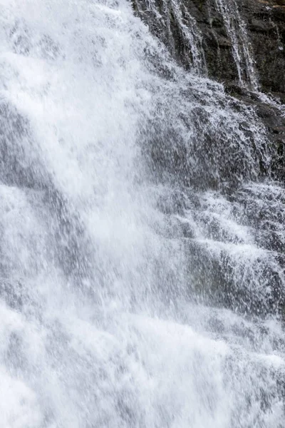 Köpüklü, beyaz bir şelalenin karanlık, sarp kayalıklardan aşağı yuvarlanışının yakın plan fotoğrafı.