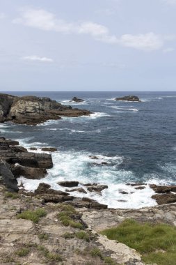 Kıyı şeridi derin mavi okyanus, açık mavi gökyüzü, ve uzakta küçük bir ada.