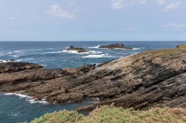 Arka planda açık mavi gökyüzünün altında okyanus olan kayalık kıyı şeridi
