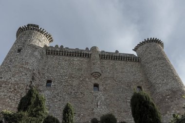 İki kulesi ve siperli bir duvarı olan taş kale, gri bulutlu bir gökyüzüne karşı duruyor, Guadalajara İspanya 'da yeşilliklerle çevrili.