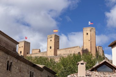 Her birinin üzerinde kırmızı ve sarı bayraklar ve mavi ve beyaz olan üç kuleli taş kale, Molina de aragon bulutlu mavi bir gökyüzüne karşı duruyor.