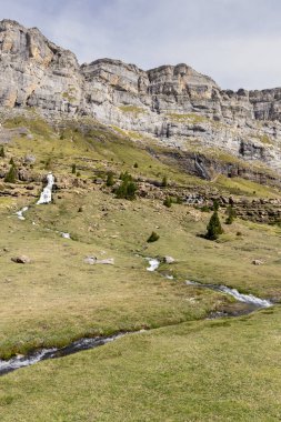 Kayalık dağlarla, yemyeşil otlarla ve berrak bir gökyüzünün altında kıvrımlı derelerle sakin bir manzara.