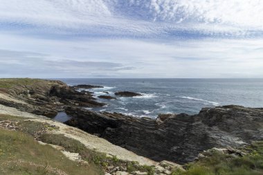 Kayalık kayalıklarla, çalkantılı denizlerle ve desenli bulutlarla süslenmiş gökyüzüyle manzaralı kıyı manzarası.