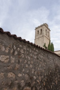 Arkasında tarihi bir kule olan parçalı bulutlu bir gökyüzünün altında dokulu taş bir duvar.
