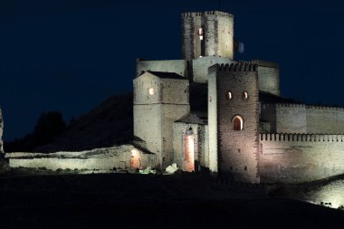 Ortaçağ şatosu gece aydınlandı, karanlık gökyüzüne karşı taş duvarlarını ve kulelerini aydınlattı.
