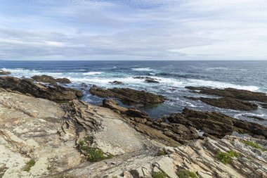 Güzel kayalık kıyı şeridi parçalı bulutlu bir gökyüzü altında dalgalar halinde, dingin ve doğal bir güzellik yayıyor.
