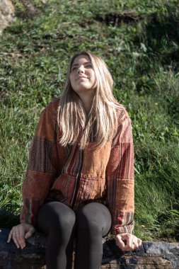 Güzel sarışın kadın taş duvarda mutlu bir şekilde oturuyor.