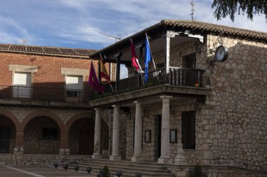Kemerleri, bayrakları, saati ve bulutlu gökyüzünün altında bir balkon olan taş bina.